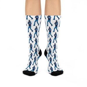 May include: A pair of white socks with a repeating pattern of a person wearing a blue denim jacket and jeans. The socks have black toes and heels.