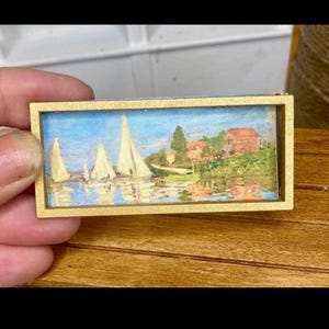 Può includere: Piccolo dipinto rettangolare in una cornice dorata. L'opera raffigura barche a vela su un lago con una casa e alberi sullo sfondo. Il dipinto ha un cielo blu e acqua con barche a vela bianche.