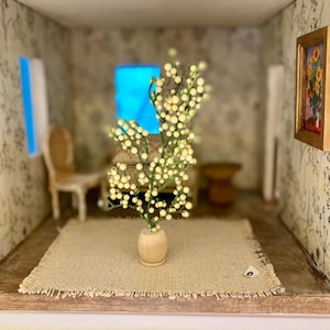 May include: Miniature dollhouse interior with a beige rug, a wooden vase holding a plant with white berries, and a small painting with a gold frame. The walls are decorated with floral wallpaper.