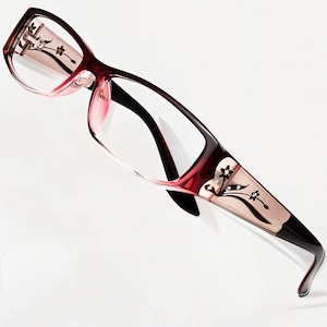 May include: Red and black eyeglasses with a floral design on the side. The glasses have a clear lens and a delicate floral pattern with rhinestones.