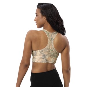 Könnte beinhalten: Ein beiger Sport-BH mit Kartenmuster. Der BH hat einen Racerback-Stil und besteht aus einem weichen, dehnbaren Material. Das Kartenmuster weist grüne und braune Details auf.