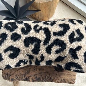 Könnte beinhalten: Ein beige-schwarzes Kissen mit Leopardenmuster und flauschigem Stoff.