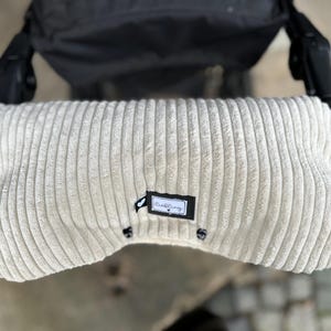 Könnte beinhalten: Ein beigefarbener Kinderwagenlenkerbezug aus Cord mit einem schwarzen Etikett mit der Aufschrift "CuddleBug".