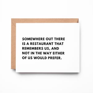 May include: A white rectangular greeting card with black text that reads: SOMEWHERE OUT THERE IS A RESTAURANT THAT REMEMBERS US, AND NOT IN THE WAY EITHER OF US WOULD PREFER. The card is partially tucked into a light brown kraft paper envelope.