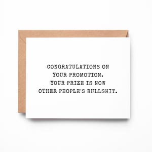 May include: A white rectangular greeting card with black typewriter-style text that reads: CONGRATULATIONS ON YOUR PROMOTION. YOUR PRIZE IS NOW OTHER PEOPLE'S BULLSHIT. The card is partially tucked into a plain light brown kraft paper envelope.