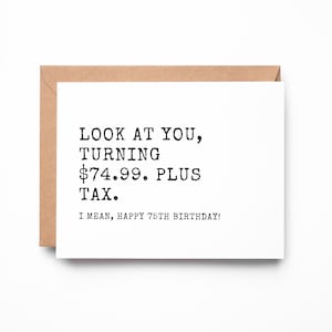 May include: A white rectangular greeting card with a brown envelope behind it. The card features black typewriter-style text that reads: LOOK AT YOU, TURNING $74.99. PLUS TAX. I MEAN, HAPPY 75TH BIRTHDAY! The design is centered on the card.