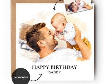 May include: A square greeting card featuring a watercolour-style illustration of a parent lifting a baby. The text "HAPPY BIRTHDAY DADDY" is printed below the image. A small inset photo shows the original reference image of the pair.