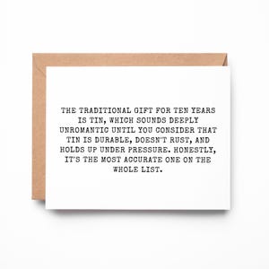 May include: A white greeting card with black typewriter-style text that reads: THE TRADITIONAL GIFT FOR TEN YEARS IS TIN, WHICH SOUNDS DEEPLY UNROMANTIC UNTIL YOU CONSIDER THAT TIN IS DURABLE, DOESN'T RUST, AND HOLDS UP UNDER PRESSURE. HONESTLY, IT'S THE MOST ACCURATE ONE ON THE WHOLE LIST. The card is placed against a brown envelope.