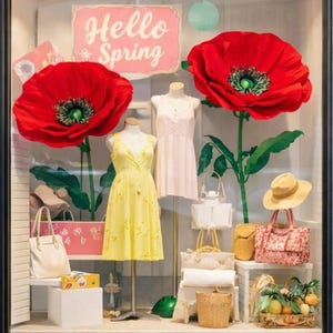 May include: A storefront display featuring a "Hello Spring" sign and large red poppy decorations. Two mannequins showcase yellow and pink dresses. Accessories include handbags, a straw hat, and a basket of oranges.