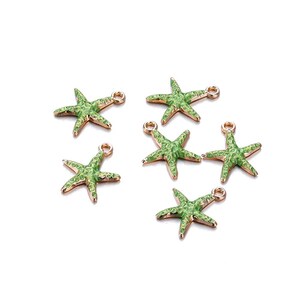 Könnte beinhalten: Sechs grüne Seestern-Anhänger mit goldfarbenen Rändern und Schlaufen zur Schmuckherstellung. Die Anhänger sind auf einer weißen Oberfläche verstreut. Ideal für die Herstellung von Schmuck mit Meeresthema.