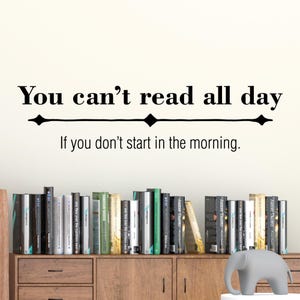 May include: A black and white wall decal with the text "You can't read all day If you don't start in the morning." The decal is above a bookshelf filled with books.