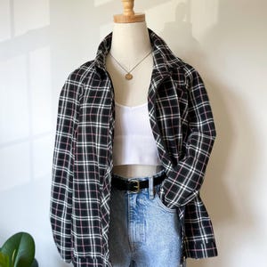 May include: A black and white checked jacket with pink detailing, paired with a white top and light blue jeans. The jacket is zipped up and displayed on a mannequin. A black belt with a gold buckle is also visible.