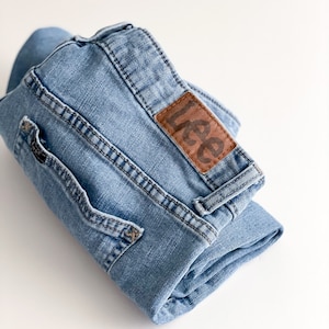 May include: A pair of blue denim jeans folded in half, with a brown leather patch that says "Lee" on the back pocket.