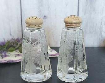 May include: A pair of clear glass salt and pepper shakers with etched grapevine designs and wooden tops.