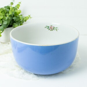 May include: A round ceramic bowl with a smooth, solid light blue exterior and a white interior. The inner rim features a small, delicate floral decal depicting a single pink rose with green leaves. The bowl has a simple, clean design.