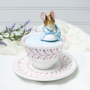 May include: A white ceramic mug with a black handle and the text "But First, Coffee" in a bold, black font. The mug is set against a blurred background, suggesting a cozy setting.