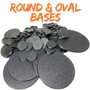 Può includere: Un assortimento di basi rotonde e ovali nere con superficie strutturata. Le basi sono di varie dimensioni, con il testo arancione "ROUND & OVAL BASES". Adatto per miniature o modellini.