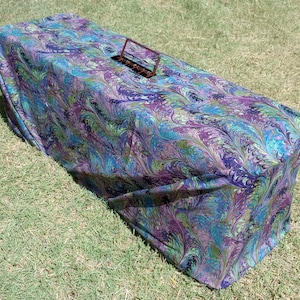 May include: A long, rectangular, covered box with a marbled pattern in shades of purple, blue, and green. The box has a metal handle on top.