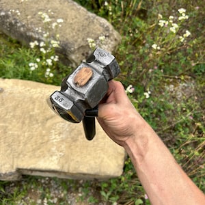 May include: A heavy-duty, dark gray metal sledgehammer with a wooden striking face and a black handle. The number "36" is stamped on the head. The tool is designed for heavy-duty construction or demolition work.