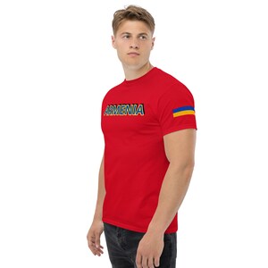 May include: Red t-shirt with the word "ARMENIA" printed in yellow and blue letters. The shirt has a blue and yellow stripe on the right sleeve, resembling the Ukrainian flag.