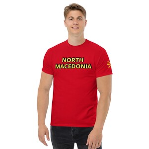 May include: A red t-shirt with the words "NORTH MACEDONIA" in black and yellow lettering. The flag of North Macedonia is on the right sleeve. The shirt is made of a soft material.