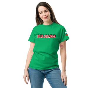 Może przedstawiać: Zielony T-shirt z nadrukiem słowa "BULGARIA" w czerwonych i czarnych literach. Prawy rękaw ma wzór flagi bułgarskiej.