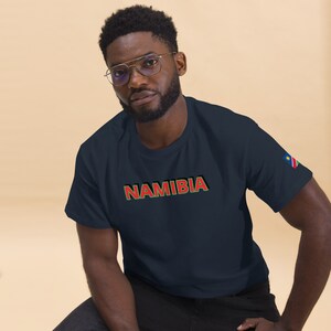 May include: A navy blue t-shirt with the word "NAMIBIA" in red and green letters. The Namibian flag is on the right sleeve.