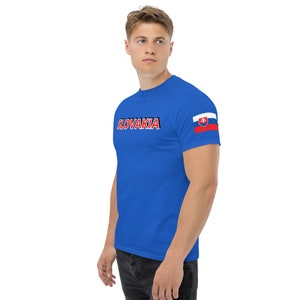 May include: Royal blue t-shirt featuring the word "SLOVAKIA" in white, outlined in red and black, across the chest. The Slovakian flag is on the left sleeve. The shirt is made of a soft material.