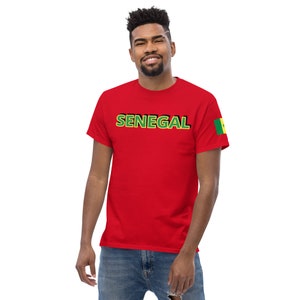 May include: A red t-shirt with the word "SENEGAL" in green and black lettering across the chest. The Senegal flag is on the left sleeve. The shirt is worn by a person.