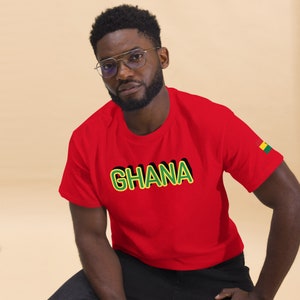 May include: Red t-shirt with a yellow and green outline of the word "GHANA" printed on the front. A small green, yellow, and red flag is on the right sleeve.