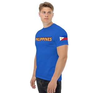 May include: A royal blue t-shirt with the word "PHILIPPINES" printed in yellow and red on the front. The right sleeve features a small Philippine flag.