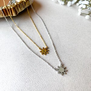 K&ouml;nnte beinhalten: Zwei goldene und silberne Halsketten mit einem Sonnenanh&auml;nger. Die goldene Halskette hat einen kleinen Buchstaben "K" auf dem Sonnenanh&auml;nger. Die silberne Halskette hat einen gr&ouml;&szlig;eren Sonnenanh&auml;nger.