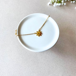 K&ouml;nnte beinhalten: Eine goldene Halskette mit einem Sonnenanh&auml;nger. Der Anh&auml;nger ist eine stilisierte Sonne mit acht Strahlen und einem Buchstaben "K" in der Mitte.