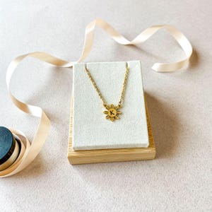 K&ouml;nnte beinhalten: Goldkette mit einem Sonnenanh&auml;nger mit dem Buchstaben K. Die Kette wird auf einem wei&szlig;en und h&ouml;lzernen Pr&auml;sentationsst&auml;nder pr&auml;sentiert.