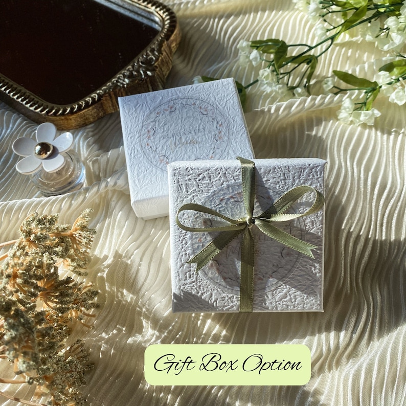 K&ouml;nnte beinhalten: Zwei wei&szlig;e Geschenkboxen mit einem gr&uuml;nen Band, das zu einer Schleife gebunden ist. Die Box rechts ist geschlossen und die Box links ist offen. Die Boxen haben eine strukturierte Oberfl&auml;che und ein Blumenmuster.