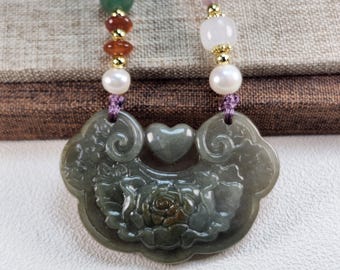 Puede incluir: Un collar con colgante de jade con un diseño floral y un acento en forma de corazón. El collar presenta un cordón morado con varias cuentas, incluyendo perlas, y piedras verdes, rojas y blancas. El colgante es de color verde apagado.