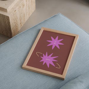 May include: A rectangular wooden frame containing a dark red print with two purple star-shaped graphics. The top star features the text "era of light" and the bottom star features the text "alignment" with a thin gold circular line surrounding it.