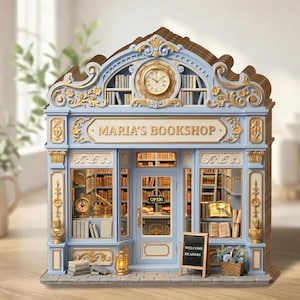 May include: A detailed miniature model of a bookstore, painted in blue and gold, with the name "MARIA'S BOOKSHOP" above the entrance. The model includes a clock, bookshelves, and a small chalkboard sign that says "WELCOME READERS".