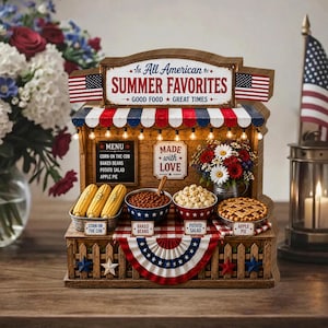 May include: A wooden miniature of an "All American Summer Favorites" food stand. It features corn on the cob, baked beans, potato salad, and apple pie. The stand is decorated with American flags and a red, white, and blue banner.