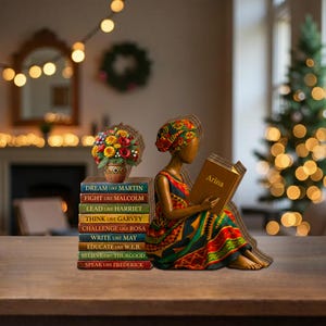 May include: A wooden figurine of a person reading a book titled "Arina", wearing a colorful dress and head wrap. Beside the figure is a stack of books with titles like "Dream Like Martin" and a vase of flowers. The scene is set on a wooden table.