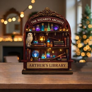 May include: A decorative wooden shelf unit with the text "THE WIZARD'S ARCHIVE" and "ARTHUR'S LIBRARY". The shelf is filled with potion bottles, books, a crystal ball, and an owl figurine. Fairy lights illuminate the shelves, creating a magical ambiance.