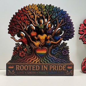 May include: A wooden sculpture featuring a rainbow-colored tree with figures reaching towards the branches. The base reads "ROOTED IN PRIDE" with the words "LOVE, UNITY, PRIDE, COMMUNITY" below. The tree's leaves and roots are in vibrant colors.