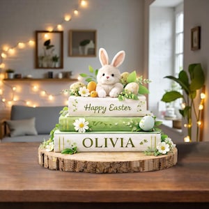 May include: An Easter display with a plush bunny, eggs, and flowers on stacked books. The books are decorated with the text "Happy Easter" and "OLIVIA". The display is set on a wooden slice, a rustic touch.