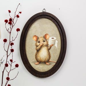 May include: An oval-framed wall art piece featuring a painting of a brown mouse holding a white roll of toilet paper. The mouse has large ears and a light-colored belly, set against a textured beige background within a dark brown wooden frame.