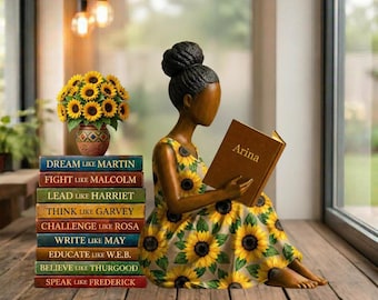 May include: A wooden figurine of a woman reading a book titled "Arina", wearing a sunflower-patterned dress. A stack of books with inspirational quotes and a vase of sunflowers are next to her. The books read: Dream Like Martin, Fight Like Malcolm, etc.