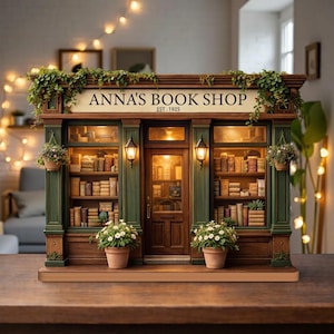Puede incluir: Una réplica en miniatura de "Anna's Book Shop" con una estética vintage. La tienda presenta una fachada de madera con detalles verdes, un letrero y una puerta. Está decorada con plantas, luces y flores en macetas, creando un ambiente acogedor.