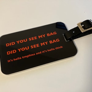 Może przedstawiać: Czarna metka bagażowa ze srebrną klamrą i czerwonym napisem "DID YOU SEE MY BAG DID YOU SEE MY BAG It's hella trophies and it's hella thick"