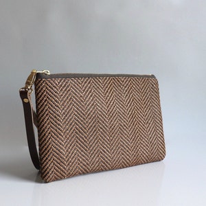May include: A brown and black woven clutch with a zipper closure and a brown leather strap.