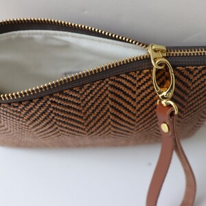 May include: A brown and black woven clutch with a gold zipper and a brown leather strap.