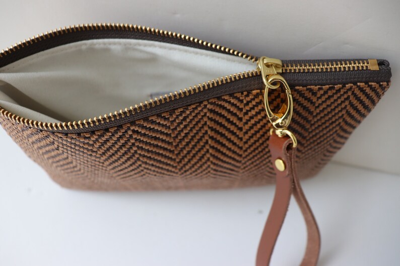 May include: A brown and black woven clutch with a gold zipper and a brown leather strap.